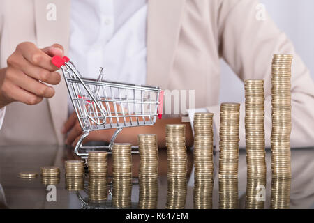 Imprenditrice con la pila di monete e piccolo carrello Foto Stock