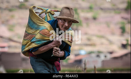 Pisac, Perù - Agosto 12 2011: Un vecchio uomo che porta una borsa pesante di cereali. Foto Stock