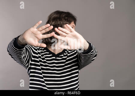 Uomo in maglione a strisce si trasforma in disparte, allungando le mani avanti. Spingere qualcuno lontano dal contatto. Guy facendo fermare la mano segno gesto palm su grigio ba Foto Stock