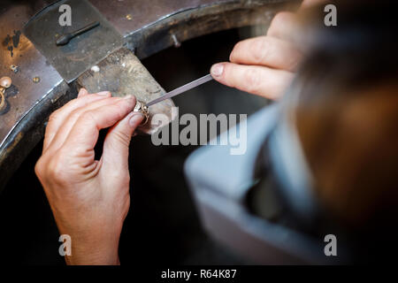 Gioielliere lavorando con un ago file un anello d'oro su un vecchio banco in autentici gioielli workshop Foto Stock