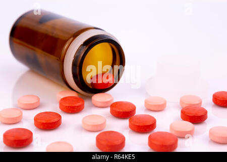 Rosso e rosa pillole e bottiglia di vetro marrone isolato su bianco superficie riflettente. Global industria farmaceutica per miliardi di dollari all'anno. Pharmace Foto Stock