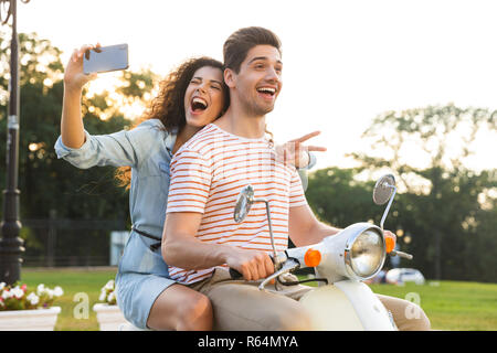 Ritratto di donna allegra tenendo selfie sullo smartphone durante la guida in moto attraverso la via della città insieme con il suo fidanzato Foto Stock