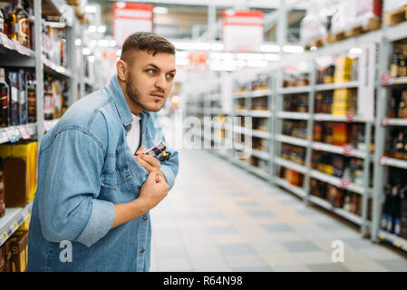 L uomo si nasconde una bottiglia di alcool sotto la sua camicia nel supermercato. Ladro maschio in negozio, marito conducendo una operazione segreta, famiglia shopping Foto Stock