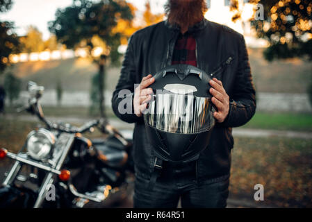 Biker maschio detiene il casco in mani, classica tritatutto sul background. Vintage bike, strada pilota e la sua moto, libertà lifestyle, Percorsi in bicicletta Foto Stock