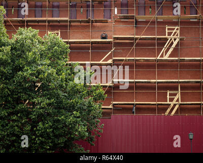 Gli sfondi e le texture: rosso muro in mattoni il rinnovamento, la costruzione lavoratore seduto solitario al ponteggio Foto Stock