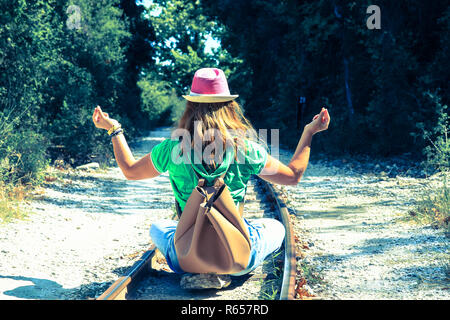 Una donna seduta con la schiena girata su binari e la pratica dello yoga. Foto Stock