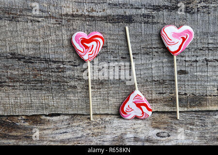 Tre bianco-rosso lecca lecca a forma di cuore su sfondo di legno Foto Stock