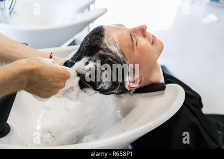 Vista di profilo di un giovane uomo di ottenere i suoi capelli lavati e la sua testa massaggiato in un salone di parrucchiere. Foto Stock
