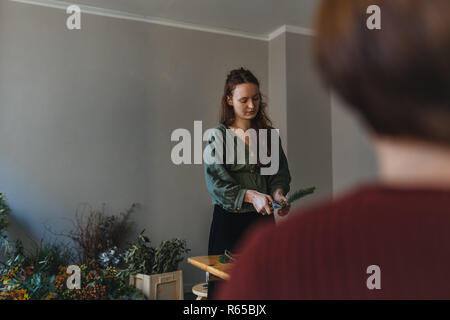 Foto di giovani caucasici fioraio chi è il taglio di un ramo di abete di fronte a un client nel proprio negozio di fiori Foto Stock