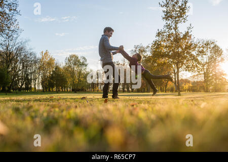 Felice giovane padre la filatura suo figlio toddler tenendo lui dalle sue mani al di fuori in autunno park. Foto Stock