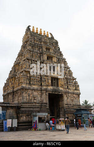 Belur, Karnataka, India - 2 Novembre 2013: pietra marrone Gopuram di ingresso principale visto da dentro il tempio contro il cielo d'argento. Cabine, segni e persone. Foto Stock