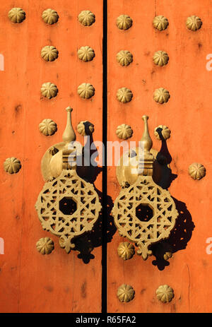 Tipico vecchio rustico di legno chiodati porta con modelli islamici su ottone doorknockers, Marocco. Foto Stock