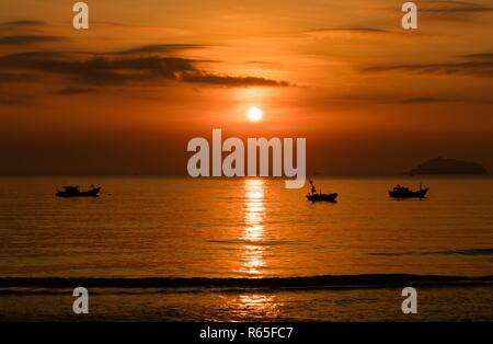 Un fiery orange sunrise sky che si affaccia sul mare della cina del sud a Vung Lam Bay Vietnam. Con un barche da pesca in silhouette. Foto Stock