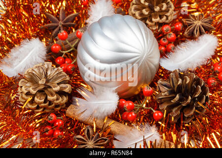 Coni di pini, bastoncini di cannella, anice stellato, piume e pallina argentata su un arancio tinsel come decorazione per il Natale Foto Stock