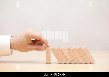 Mano d'uomo fermare l' effetto domino. Concetto di immagine per la strategia commerciale e la soluzione delle crisi. Foto Stock