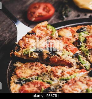 Prendere il pezzo di pizza con cucina scapola. Pizza dal forno su un vecchio tavolo di legno. Formato quadrato, effetto opaco Foto Stock