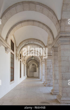 Passaggio lungo lo spostamento di prospettiva sotto arcate con colonne su un lato e un muro bianco sull'altro lato a Lisbona, Portogallo - verticale Foto Stock