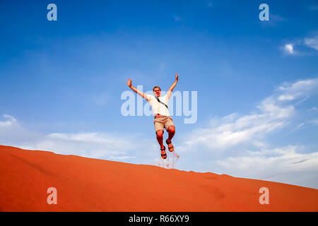 Tourist jumping over the sand dunes in Merzouga Foto Stock