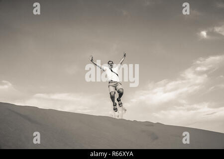 Tourist jumping over the sand dunes in Merzouga Foto Stock