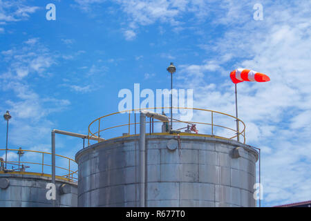 Grande serbatoio di acciaio con sostanza chimica con indicatore di direzione vento. Con il blu del cielo Foto Stock