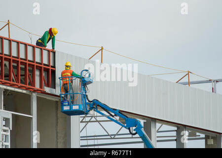 I lavoratori in cestelli sono l'installazione di lamiera, la costruzione di una fabbrica. Foto Stock