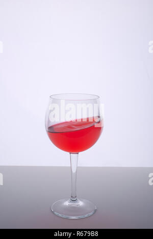 Un bicchiere con un drink rosso su una superficie bianca Foto Stock