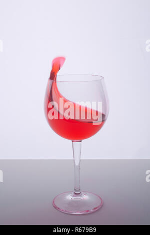 Un bicchiere con un drink rosso su una superficie bianca Foto Stock