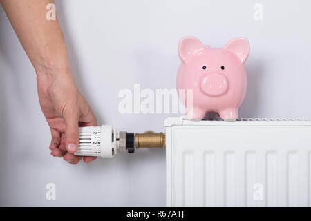 Man mano del termostato di regolazione con il salvadanaio Foto Stock