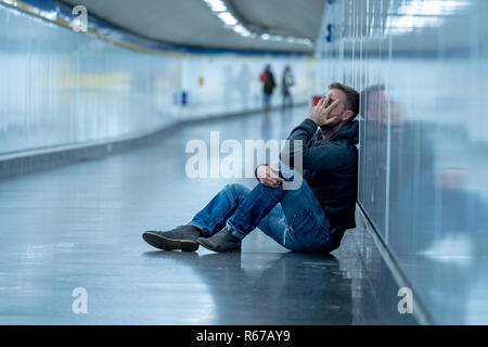 Giovane triste piangere la sofferenza della depressione stress seduta sul terreno street subway tunnel alla ricerca disperata appoggiata sulla parete da soli in disordine mentale Emo Foto Stock