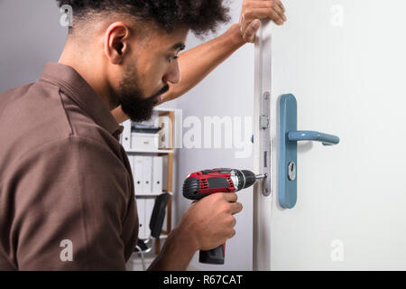 Carpenter Installazione serratura della porta con un cacciavite senza fili Foto Stock