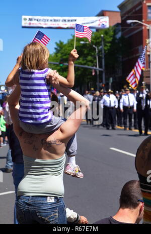 Middletown, CT, Stati Uniti d'America. Maggio 2018. Figlia seduta su mom's spalle sventola bandiera durante un giorno memoriale della celebrazione. Foto Stock