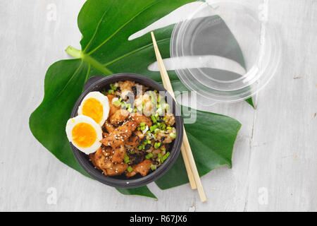 Asian prendere via cibo concetto. Due poke ciotola di riso fritto, carne di pollo, avocado e uova nella casella sul tavolo woocen vista superiore Foto Stock