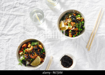 Due piatti vegetariani poke ciotola. Il tofu, riso, alghe, piselli verdi e cipolle gustosa e sana cucina vegetariana. Vista superiore laici piatta Foto Stock