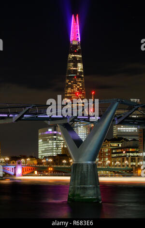 Londra, Regno Unito. 3 Dic 2018. La Shard Londra Christmas light show 2018, il Millennium Bridge è in primo piano in notturna di lunga esposizione con percorsi di luce dal passaggio di un tour in barca sul Tamigi. Il Millennium bridge è stata illuminata da luce-pittura con hand-held daylight lampade equilibrata Credito: Nigel Blake/Alamy Live News Foto Stock