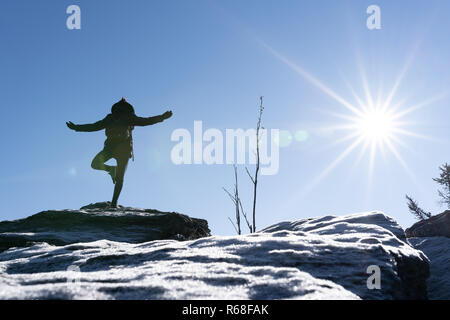 Giovane donna sta facendo yoga su un picco di montagna con ghiaccio in primo piano. Foresta Bavarese, osser, Germania. Foto Stock