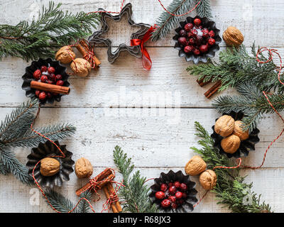 Piatto di Natale laici in forma di cerchio realizzato da sempreverdi, di bacche rosse, dadi e bastoncini di cannella in bianco sullo sfondo di legno. Spazio per il prodotto o il testo Foto Stock