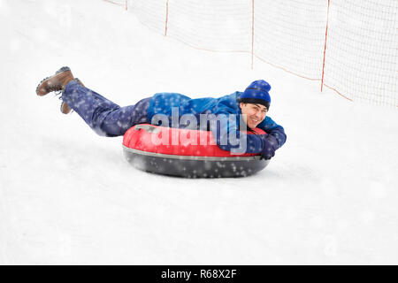 Un uomo felice lo scorrimento verso il basso sul tubo di neve in inverno. Foto Stock