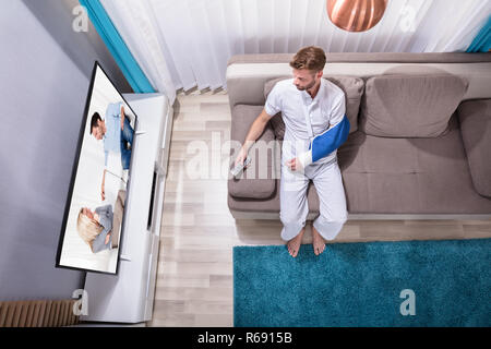 Uomo con mano fratturato di guardare la televisione Foto Stock