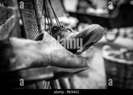 Marrone indossato scarpe in pelle con fori nelle suole, appeso sul vecchio recinto vintage con i lacci legati Foto Stock