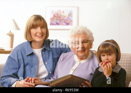 Ritratto, Indoor, 3 Generationen, Grossmutter, ihre Tochter und Enkeltochter sitzen auf dem Sofa und schauen ein Fotoalbum un Foto Stock