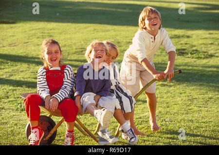 All'aperto, Parkszene, Gruppe von vier Kindern, 5-8 Jahre, spielt mit einer Schubkarre auf einer Wiese Foto Stock