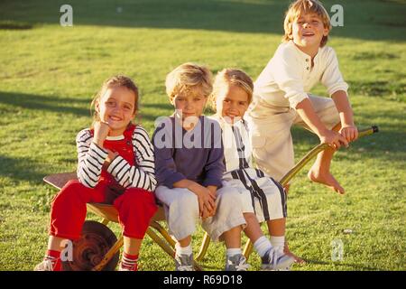 All'aperto, Parkszene, Gruppe von vier Kindern, 5-8 Jahre, sitzt in einer Schubkarre auf einer Wiese Foto Stock