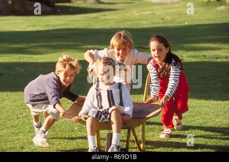 All'aperto, Parkszene, Gruppe von vier Kindern, 5-8 Jahre, spielt mit einer Schubkarre auf einer Wiese Foto Stock