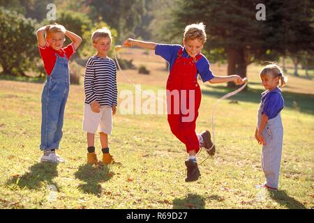 All'aperto, Parkszene, Gruppe von vier Kindern, 5-8 Jahre, auf einer Wiese, ein Junge Seilchen springt Foto Stock