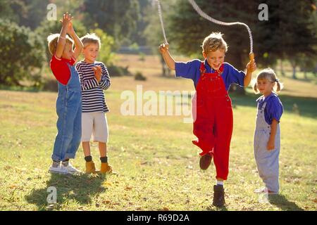 All'aperto, Parkszene, Gruppe von vier Kindern, 5-8 Jahre, auf einer Wiese, ein Junge Seilchen springt Foto Stock