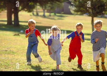 All'aperto, Parkszene, Gruppe von vier Kindern, 5-8 Jahre, laeuft lachend ueber eine Wiese Foto Stock
