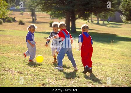 All'aperto, Parkszene, Gruppe von vier Kindern, 5-8 Jahre, spielt Mit einem gelben sfera auf einer Wiese Foto Stock