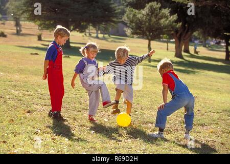 All'aperto, Parkszene, Gruppe von vier Kindern, 5-8 Jahre, spielt Mit einem gelben sfera auf einer Wiese Foto Stock