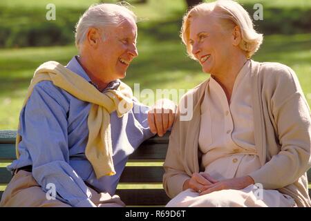 Parkszene, Outdoor, Ritratto, Halbfigur, Seniorenpaar bekleidet mit heller Kleidung unterhaelt sich auf einer Parkbank Foto Stock