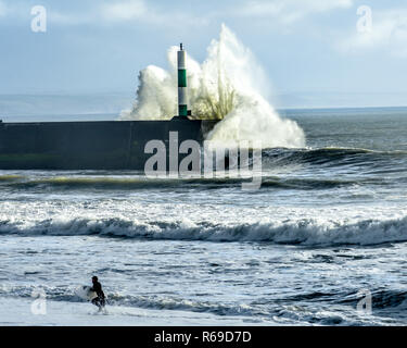 Surfer di uscire dal mare con onde grosse in Aberystwyth Foto Stock